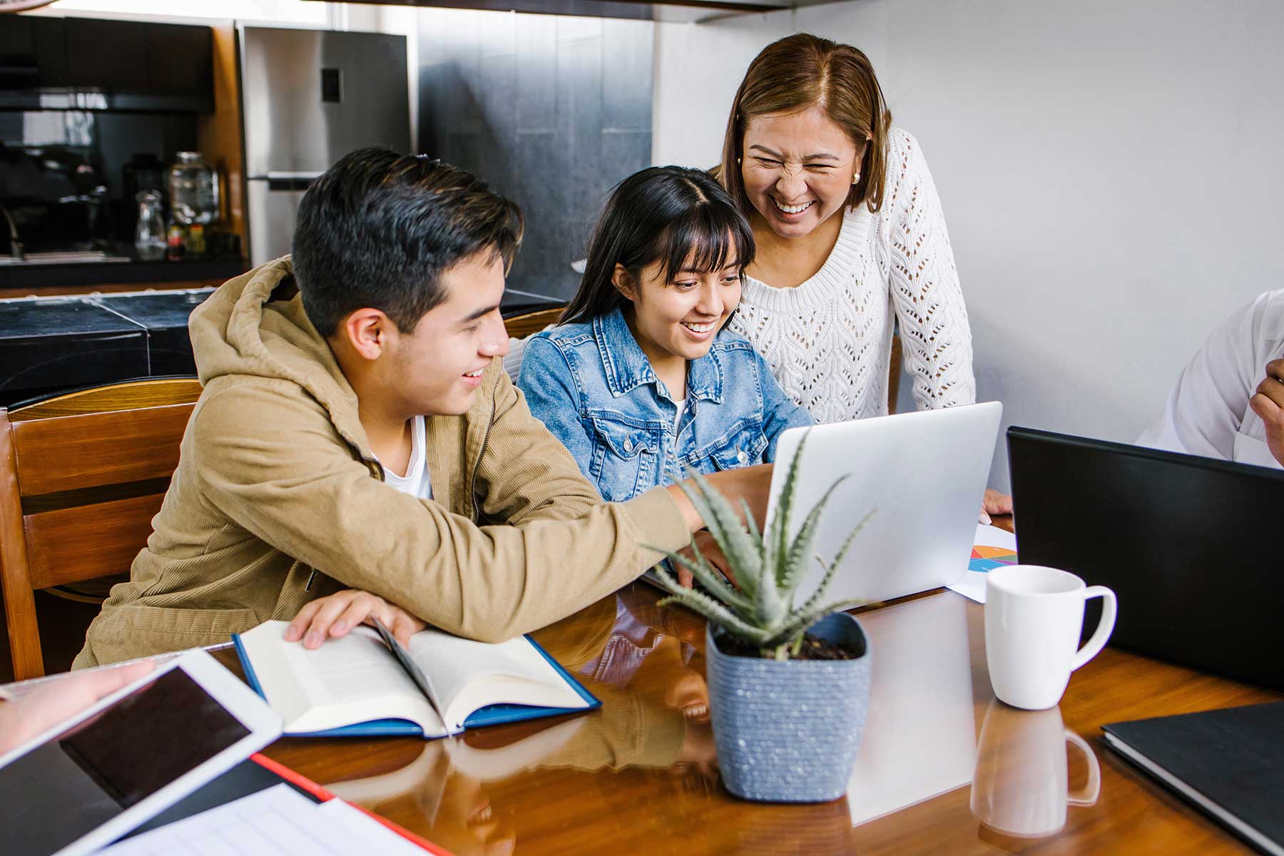 An adult and two children sitting in their kitchen looking at a laptop.