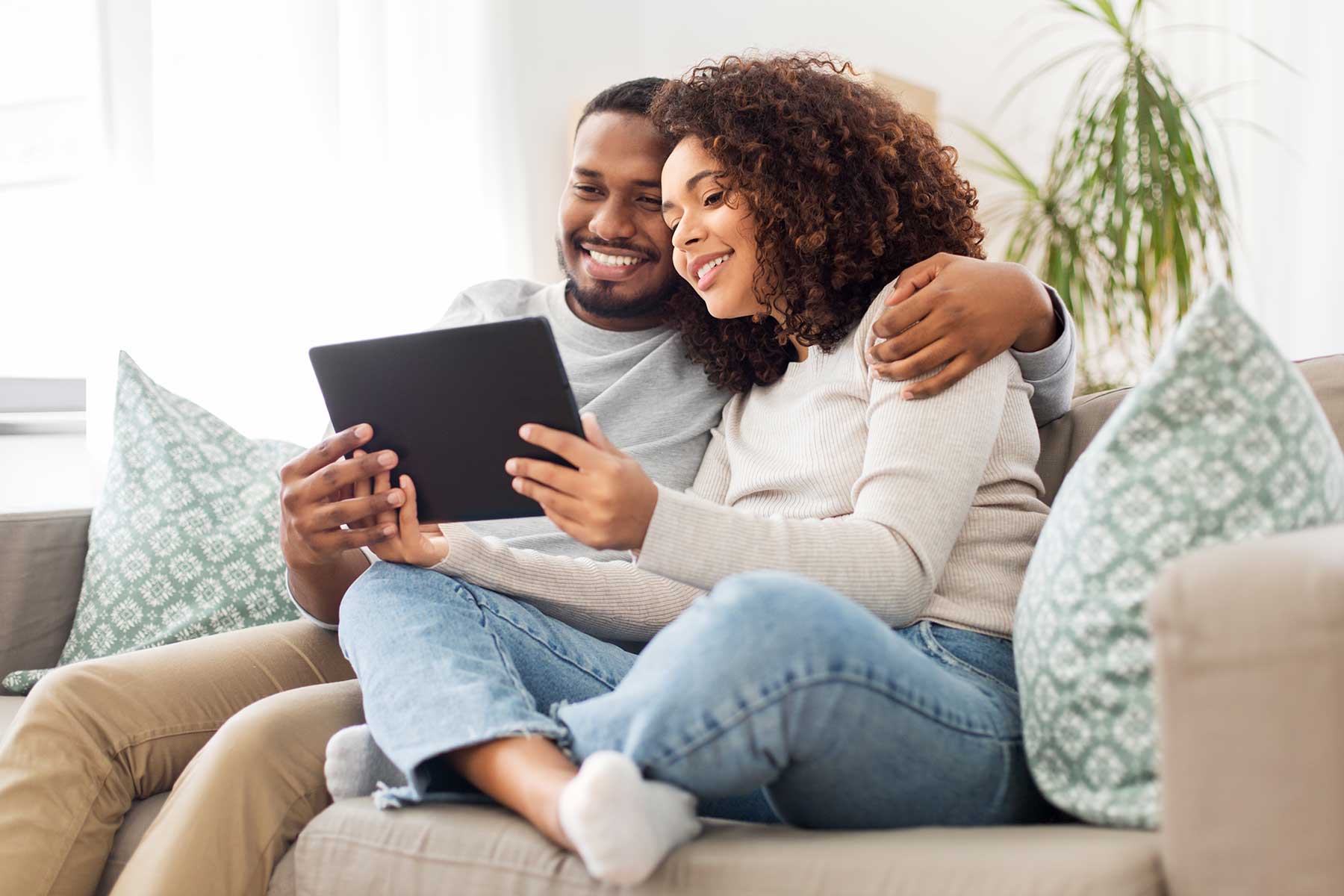 A couple sitting on a couch holding a tablet.