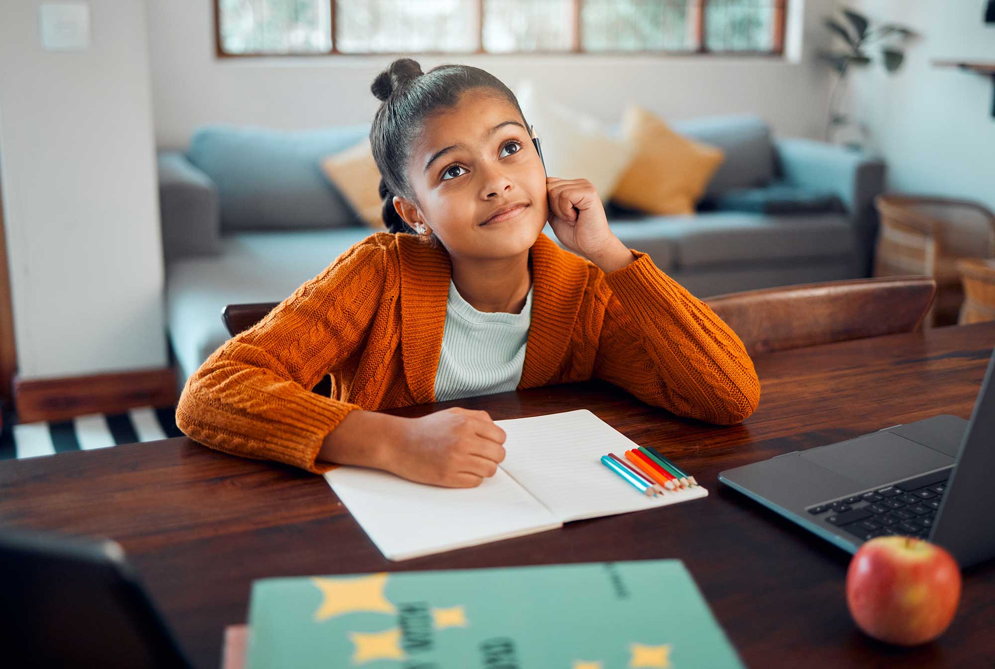 Young child sitting at a desk with a notepad and colored pencils.