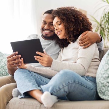 A couple sitting on a couch holding a tablet.