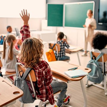 Group of students in a classroom with their hands raised.