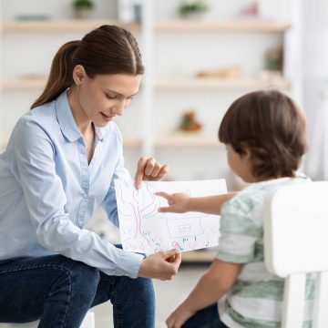 psychoeducational-testing- A child sitting in a chair pointing at a drawing being held by an adult.